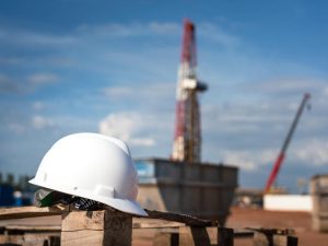 An oilfield worker safety hardhat or helmet is placed at onshore drilling rig site with blurred background of derrick structure. Ready to working in challenge industrial concept. Selective focus.